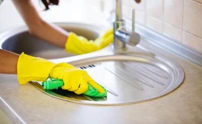Person with yellow latex gloves cleaning the kitchen sink