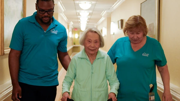 Elderly woman walking with help from staff