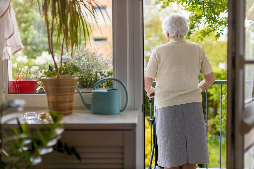 Senior woman with dementia standing near an open doorway at home, wandering in dementia and home safety concerns