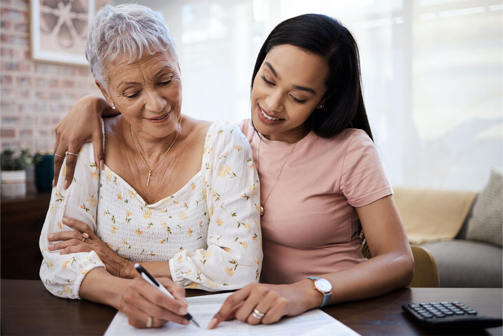 Adult daughter helping her senior mother review home care paperwork at a table
