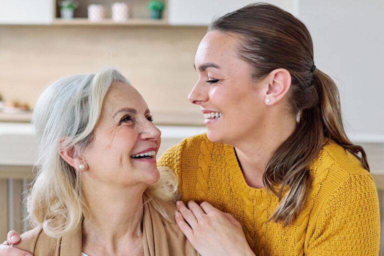 Smiling senior woman embracing her adult daughter in a bright home kitchen