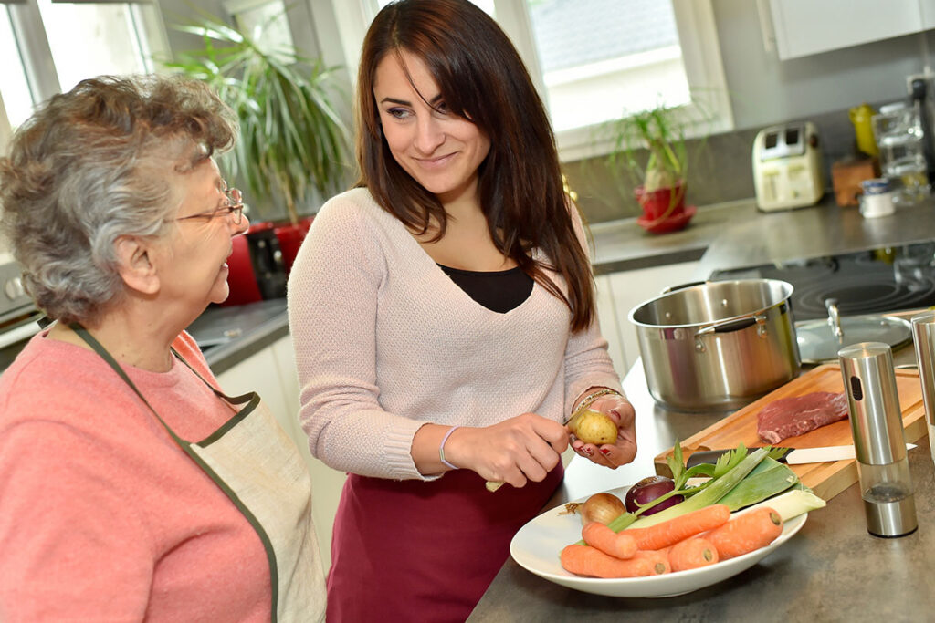 Companion and senior woman preparing vegetables together in the kitchen